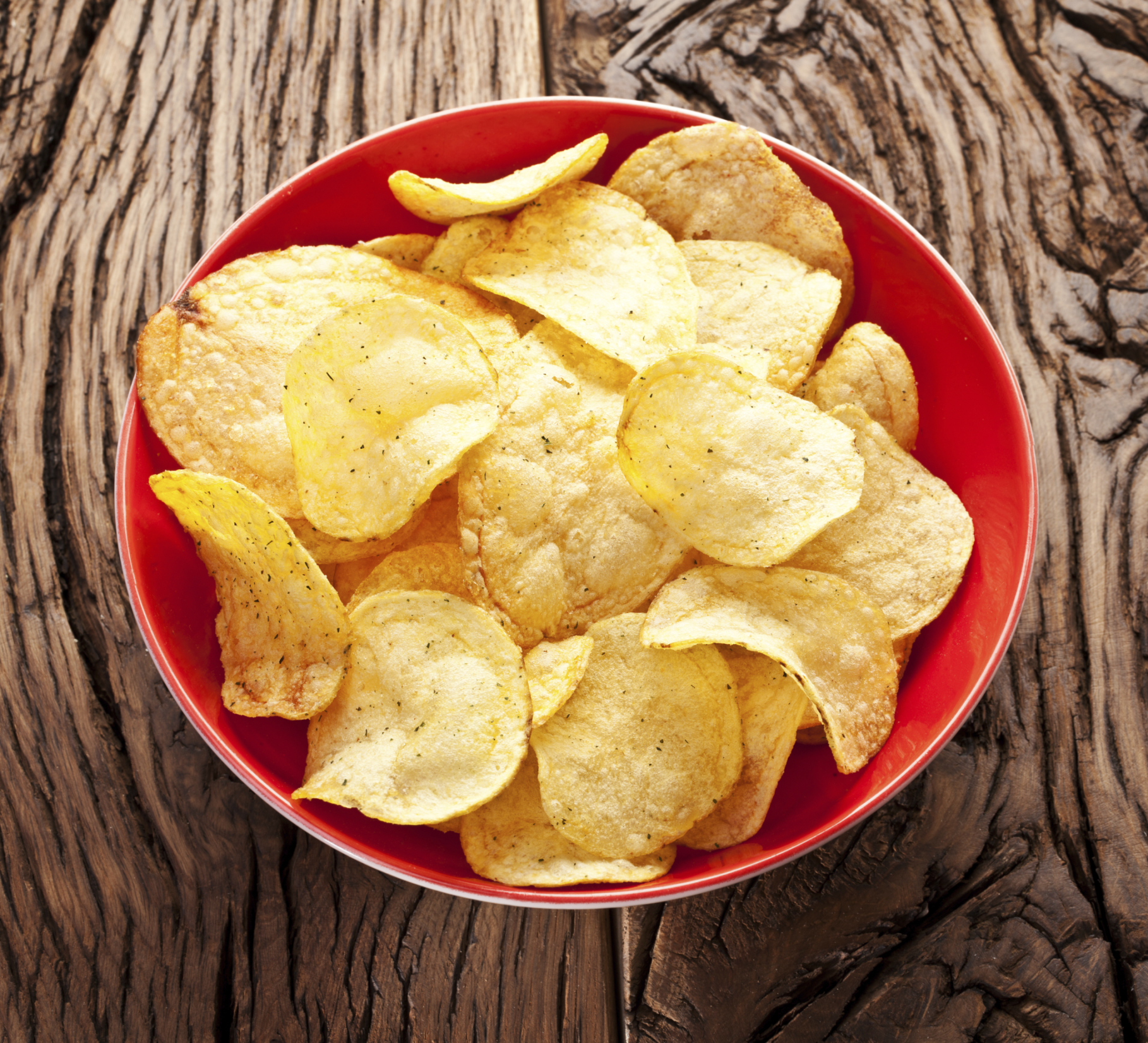 Potato chips in a bowl on old wooden table.